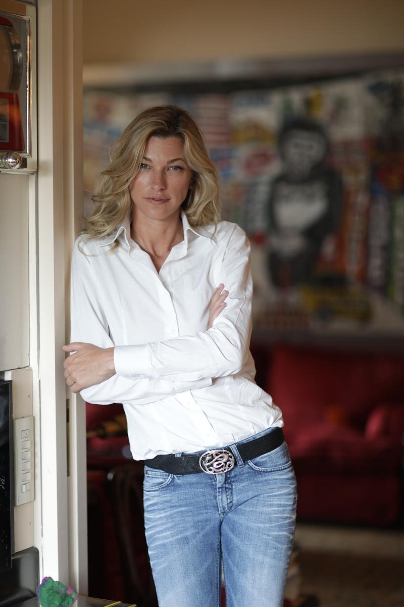 Nicole Junkerman at home in a white shirt and jeans, arms crossed in a doorway beside colourful modern art