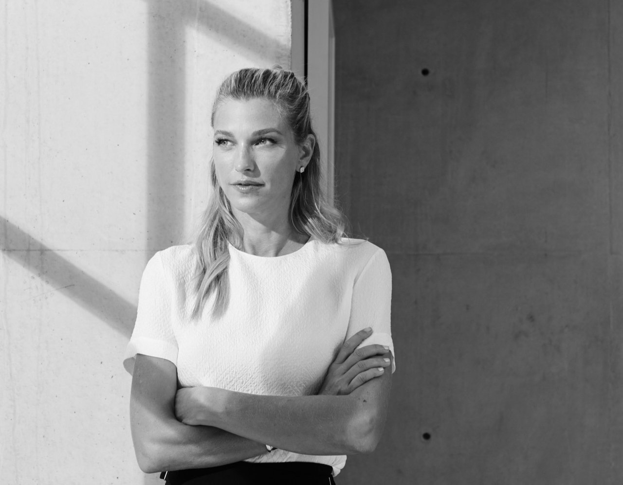 Nicole Junkerman in a cream blazer, arms crossed, against a modern concrete wall