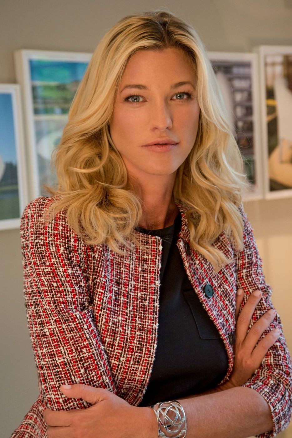 Nicole Junkerman in a tweed jacket, arms folded, framed pictures on the wall behind her